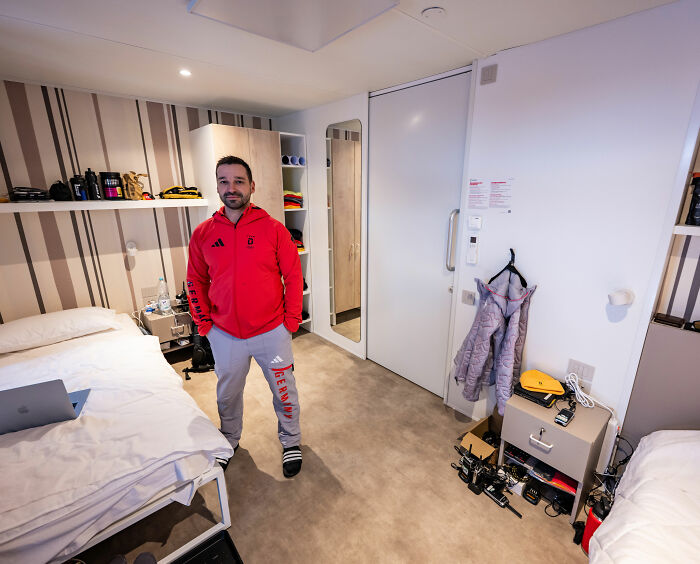 Athlete in Winter Olympics Milan rooms standing beside beds and equipment in a modern, compact athlete accommodation.