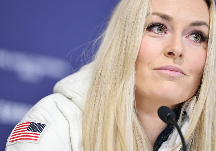 Olympian Lindsey Vonn at a press event, wearing a white jacket with an American flag patch.
