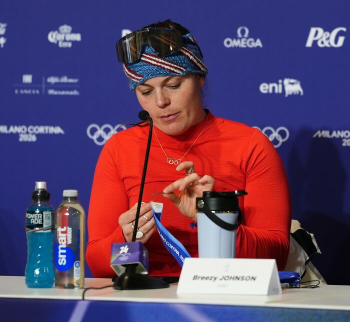 Olympian Breezy Johnson at a press conference showing a broken medal linked to the TEMU investigation.