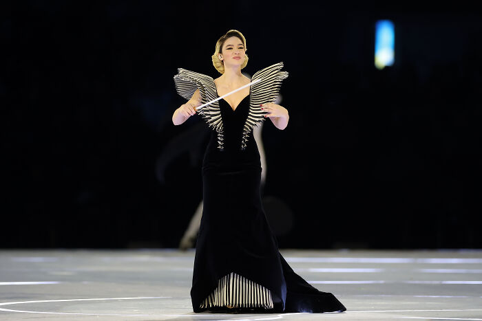 Female Winter Olympics host in an elegant black dress conducting an event before resigning after commentary sparked outrage.