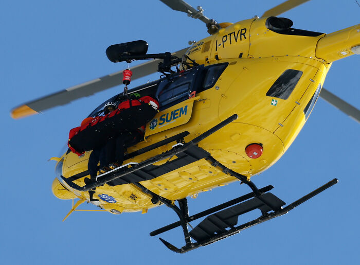 Yellow rescue helicopter mid-air with medical personnel performing an emergency lift after Lindsey Vonn crash update.