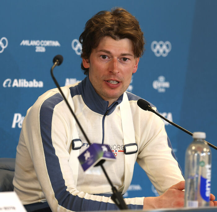 Olympian speaking at a press conference with microphones, addressing public after cheating confession.