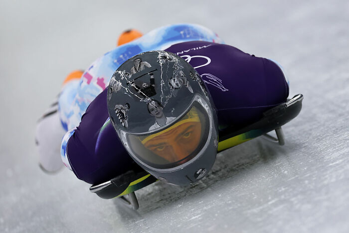 Olympic athlete in skeleton racing helmet speeding headfirst on icy track during winter Olympic sport competition.