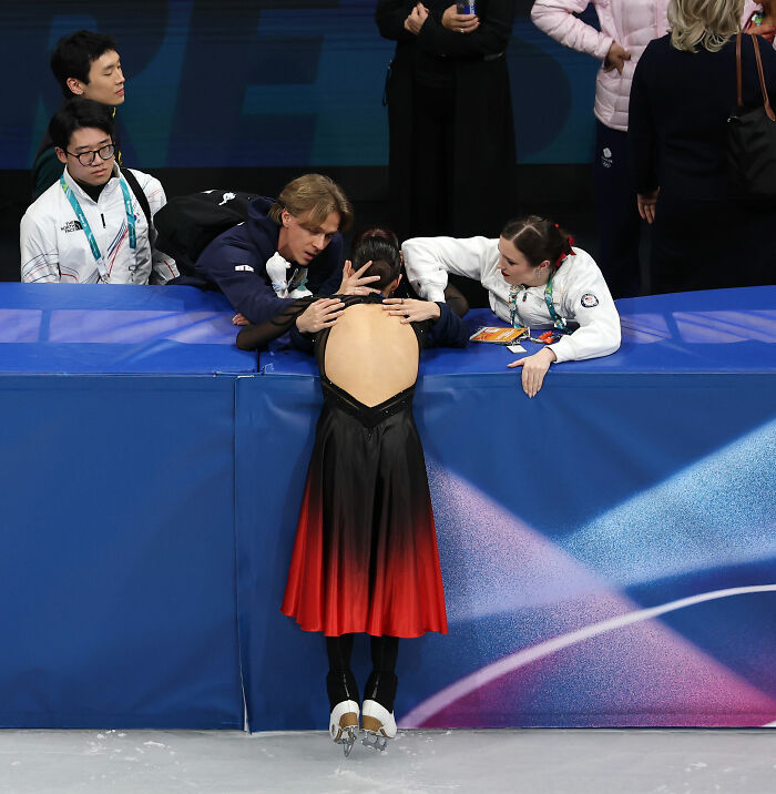 Figure skater in red and black dress receives support from US Figure Skating team after cheating scandal affecting Team USA gold medals.