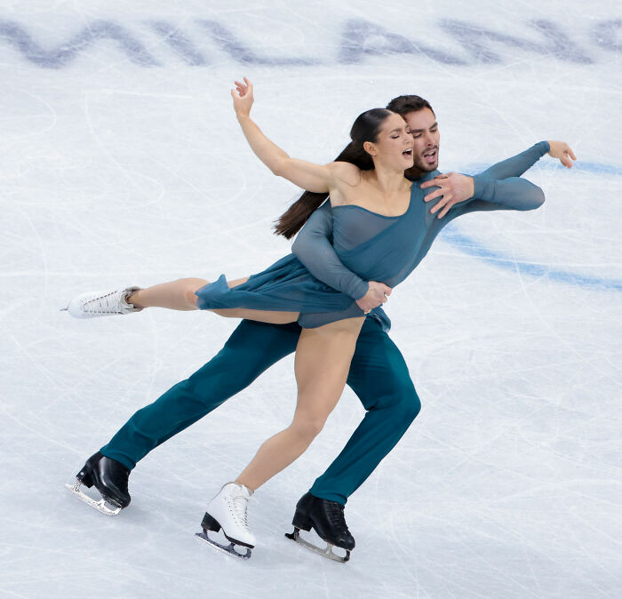 Pair of figure skaters in teal costumes performing a lift on ice, highlighting US figure skating after cheating scandal.