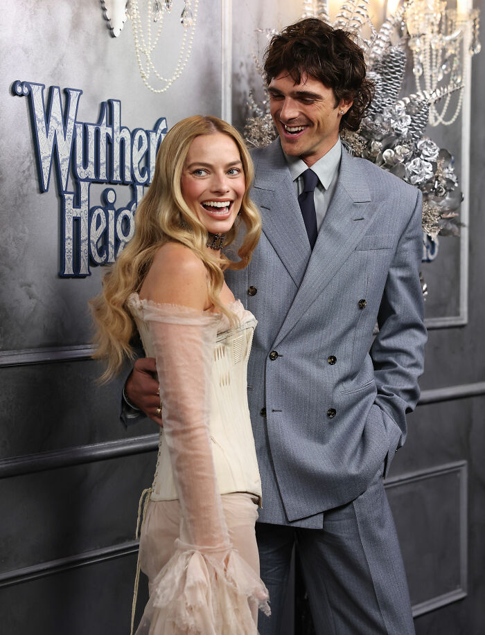 Hailey Bieber wearing lingerie-inspired outfit with sheer sleeves and corset at Wuthering Heights premiere, smiling and posing.