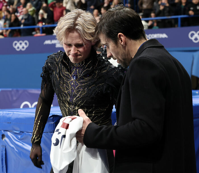 Ilia Malinin in a black costume talking to NBC Olympics president after controversial comments at Olympic event.