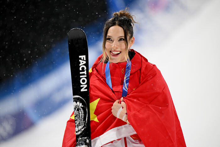 Eileen Gu wrapped in Chinese flag, holding ski, smiling after competition amid JD Vance’s comment and backlash against athlete.