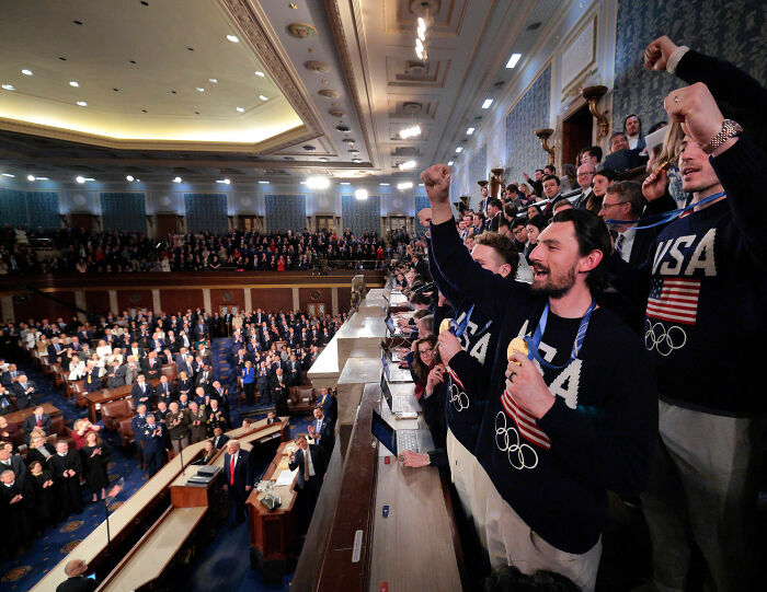 Team USA Men's Hockey players wearing Olympic sweaters, cheering passionately during a formal event at the White House. Team USA Men's Hockey players wearing Olympic sweaters, cheering passionately during a formal event at the White House.