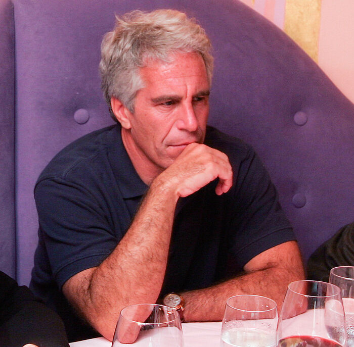 Man with gray hair sitting at restaurant table in navy shirt, related to Epstein doc and Harry Potter fans furious with JK Rowling.