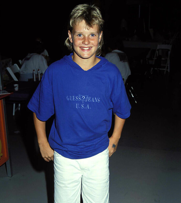 Young Zachery Ty Bryan from Home Improvement smiling in a blue Guess Jeans shirt and white pants at an indoor event.