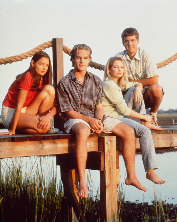 Four Dawson's Creek cast members sitting on a wooden dock by the water in a viral cringy scene discussion.