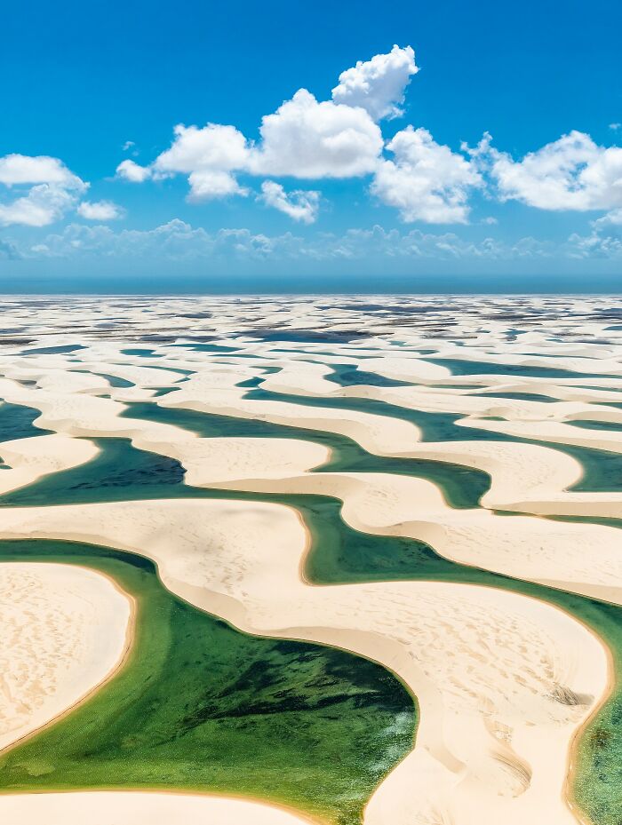 Aerial view of unusual places featuring unique sand dunes and water patterns under a bright blue sky with clouds.