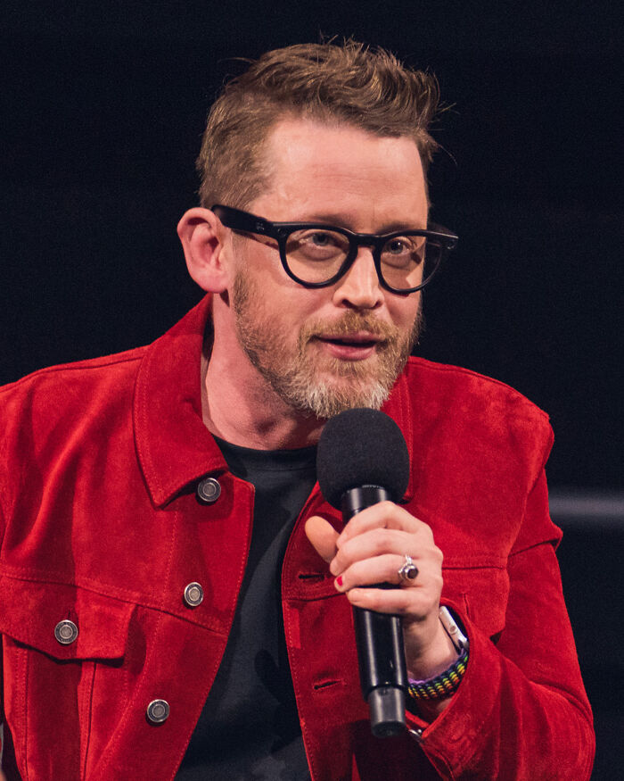 Male actor with glasses in a red jacket speaking into a microphone, representing iconic actors who dominated Hollywood.