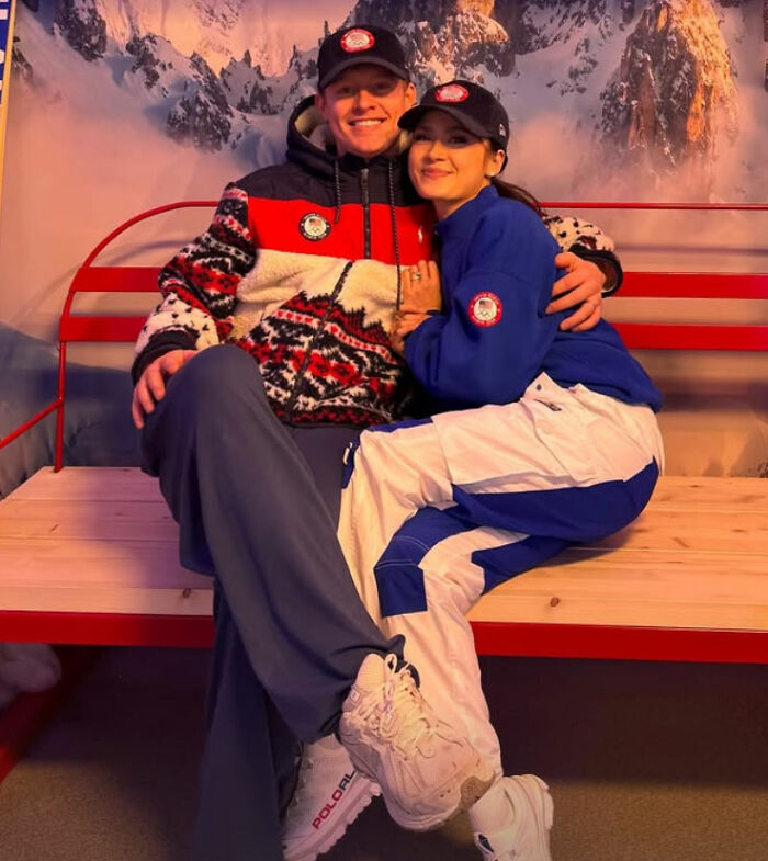 Two US figure skating athletes sitting on a bench, wearing team apparel after cheating scandal affecting gold medals.