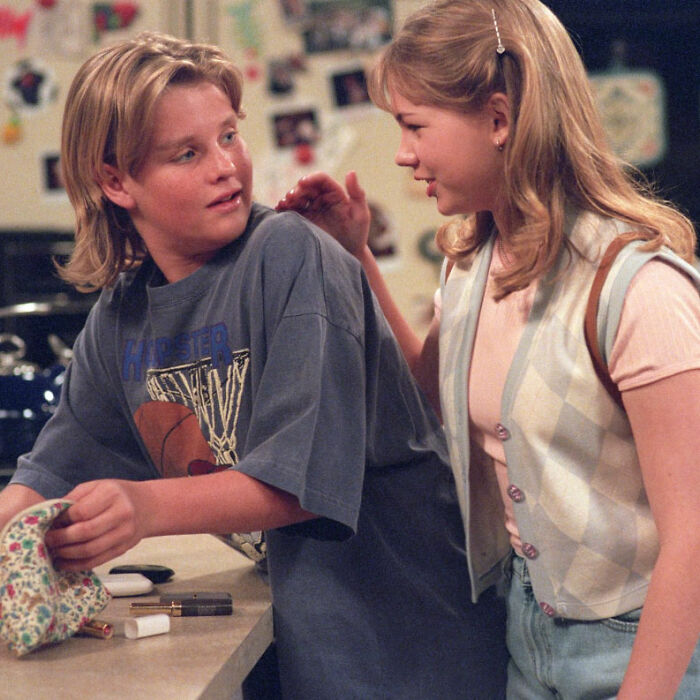 Young man and woman in casual 90s clothing, sitting and chatting in a cozy home setting, related to Home Improvement star news.