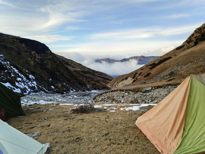 Tents pitched in a mountain valley with snow patches, illustrating spiritual tourism and travel across India.