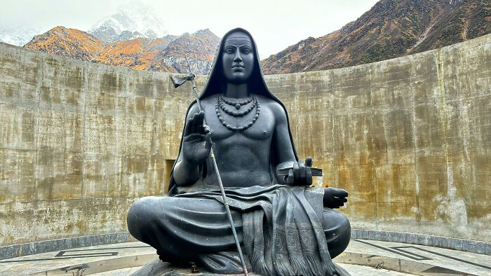 Black stone statue of a meditative figure with prayer beads in a mountainous setting, reflecting spiritual tourism in India.