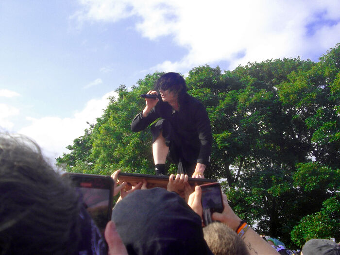 Performer in black crouching on a platform held by a crowd, illustrating unhinged and toxic ways women traumatized men.