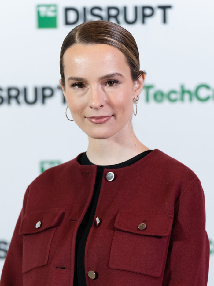 Young woman in a red jacket and hoop earrings posing at a TechCrunch Disrupt event featuring iconic actors who vanished from Hollywood.