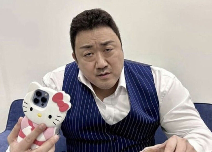 A man wearing a striped blue vest and white shirt, holding a Hello Kitty phone case, posing confidently as a gigachad.