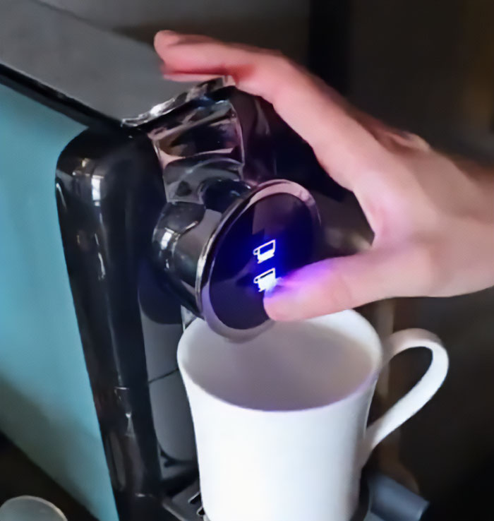 Hand pressing button on a hotel coffee machine with a white cup below related to influencer hotel hack controversy.