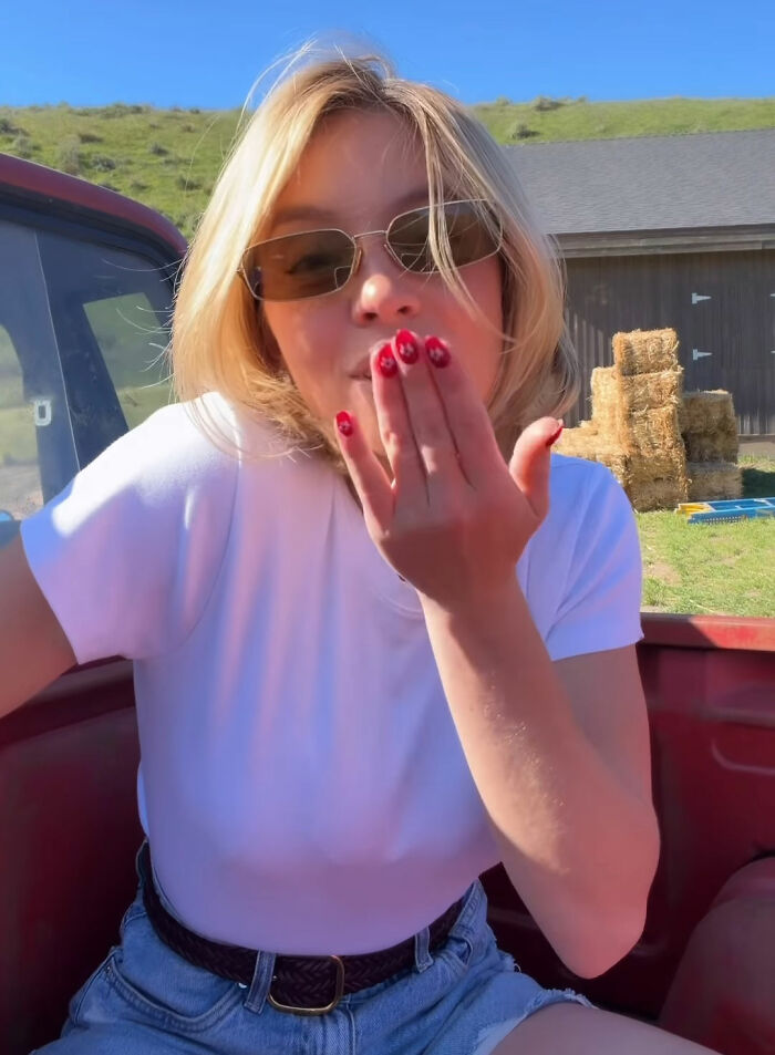 Sydney Sweeney blowing a kiss, wearing sunglasses and casual white shirt outdoors, capturing marketing promo moment.
