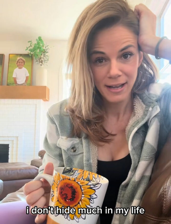 Woman in cozy jacket holding sunflower mug, responding confidently about her hotel hack for washing underwear controversy.