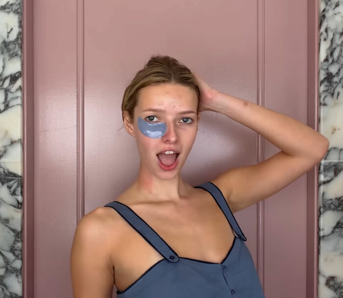 Apple Martin with under-eye mask, posing against pink wall, revealing cosmetic procedures she has had in casual attire.