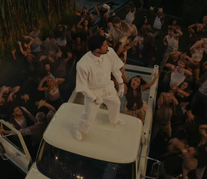 Bad Bunny standing on a vehicle surrounded by a crowd, appearing anxious before exiting Super Bowl and deleting social media.