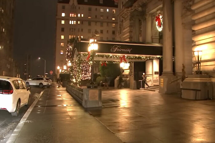 Exterior view of a ritzy hotel entrance at night with holiday decorations and street lamps lit along the sidewalk.