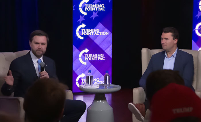 Two men seated on stage during Turning Point PAC event, discussing response after Erika Kirk changed husband's office.