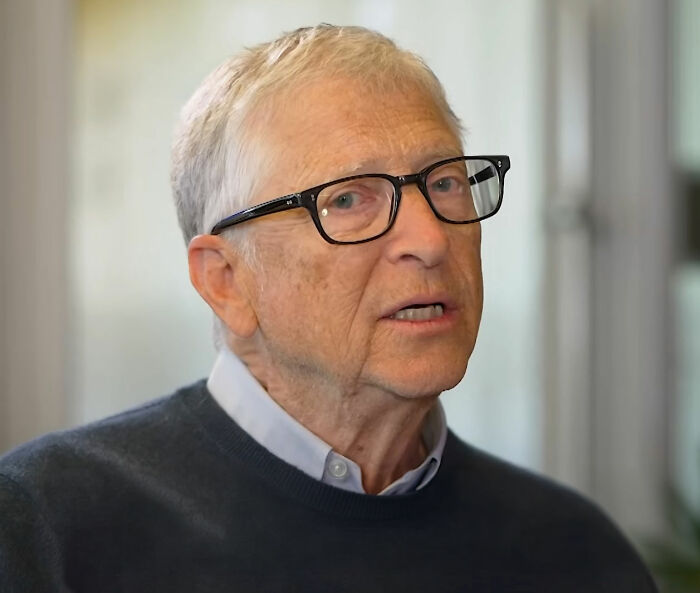 Bill Gates wearing glasses and a dark sweater speaking in an indoor setting about Epstein files.