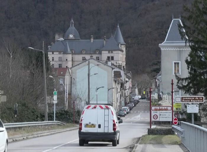 Van driving towards a small town with historic buildings, related to teacher known for helping under-privileged students.