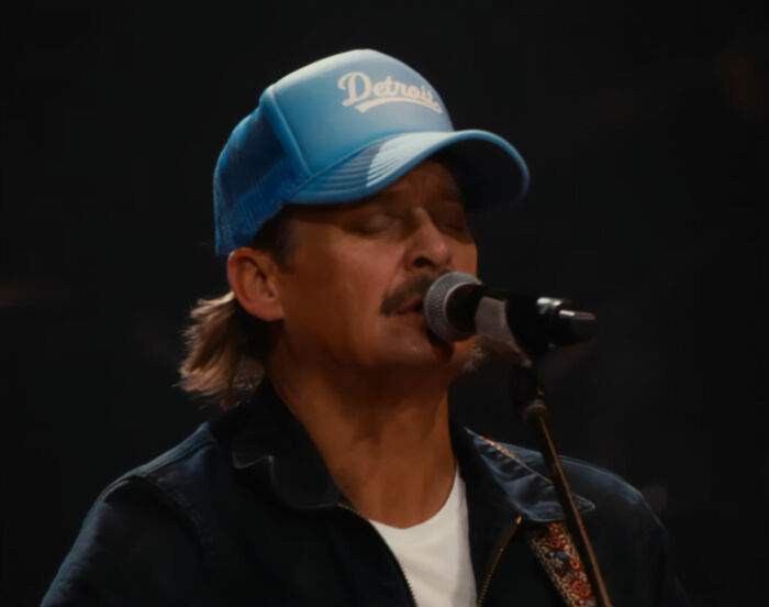 Kid Rock singing into a microphone wearing a blue Detroit cap during an alternative halftime show performance.