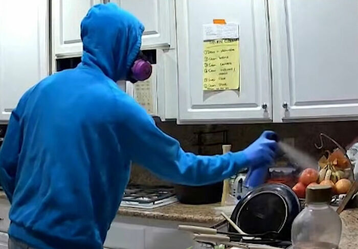 Person in a blue hoodie wearing a mask sprays disinfectant in a kitchen, linked to roommate's horrifying acts on security footage. Person in a blue hoodie wearing a mask sprays disinfectant in a kitchen, linked to roommate's horrifying acts on security footage.