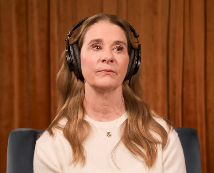 Woman with headphones in a podcast setting, discussing Bill Gates and Epstein files in a serious tone.