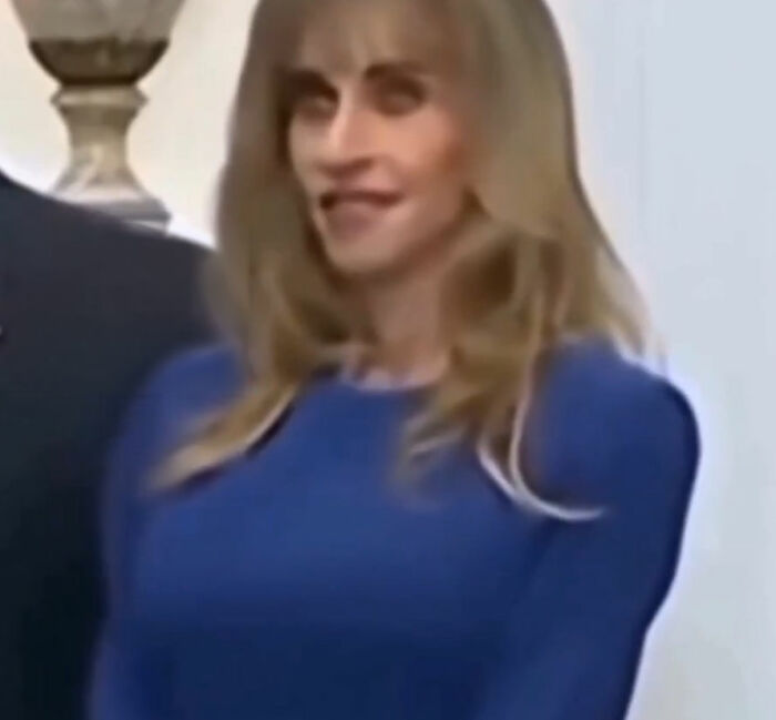 Woman displaying strange behavior during White House press conference, wearing a blue dress and smiling awkwardly.