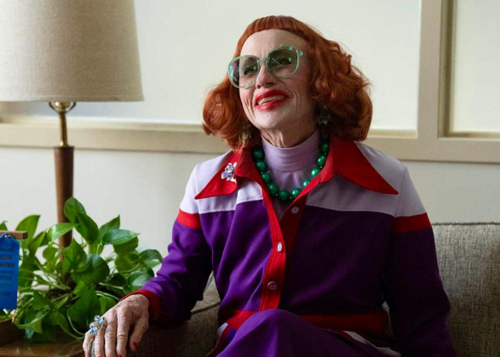 Older woman with red hair and green glasses sitting on a couch, representing Oscar nominated movies 2026.