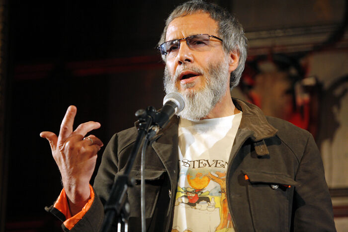 Man with gray beard and glasses speaking into a microphone, representing celebrities falsely accused of horrible crimes.