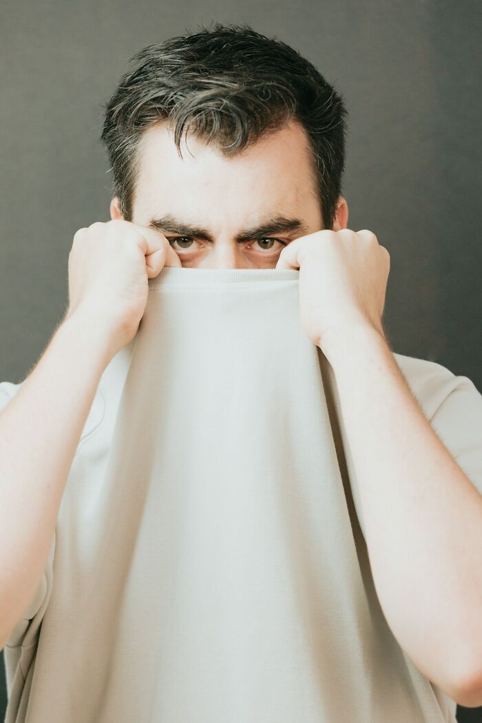 Man covering face with shirt, expressing discomfort and trauma caused by unhinged toxic behavior from women.