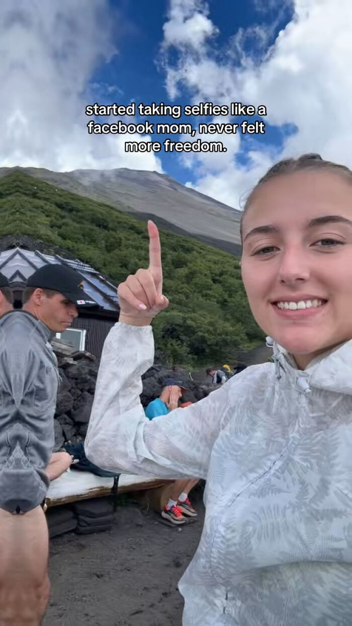 Young woman smiling and taking a hilarious selfie outdoors, capturing the chaotic energy of a mom on social media.