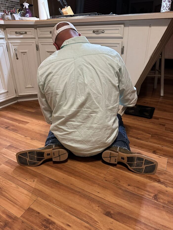Man sitting awkwardly on kitchen floor with legs splayed out, displaying hilariously awkward body language giving the ick.