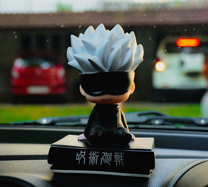 Small anime figure with spiky white hair and black blindfold sitting on a book inside a car, bf confession younger sister trouble.