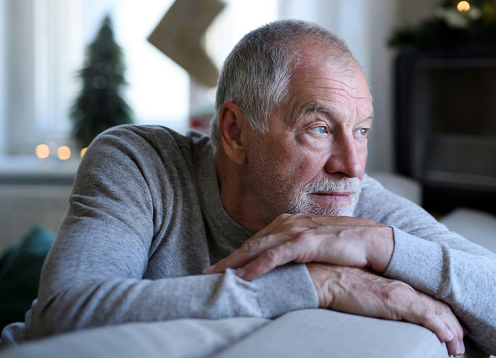 Elderly man in a gray sweater looking contemplative indoors, reflecting drama over last name and spending time with bio dad