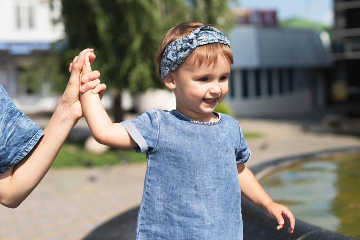Toddler girl in blue dress holding adult hand outdoors, highlighting tense family dynamics with BF&rsquo;s kids and ex involved.