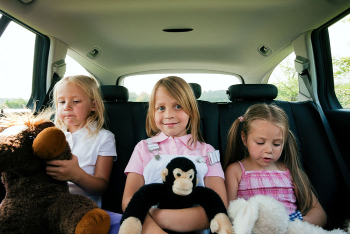 Three young girls sitting in the backseat of a car holding stuffed animals, illustrating arrogant mistress with her boyfriend&rsquo;s kids.
