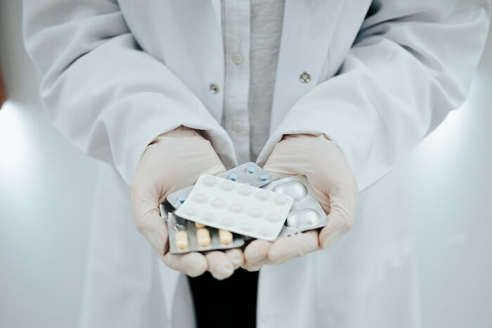 Person in a white coat wearing gloves holding multiple blister packs of pills representing dangerous things often dismissed.