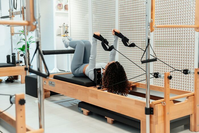 Woman exercising on Pilates reformer machine, symbolizing relief from toxic workplace moments and stress management.