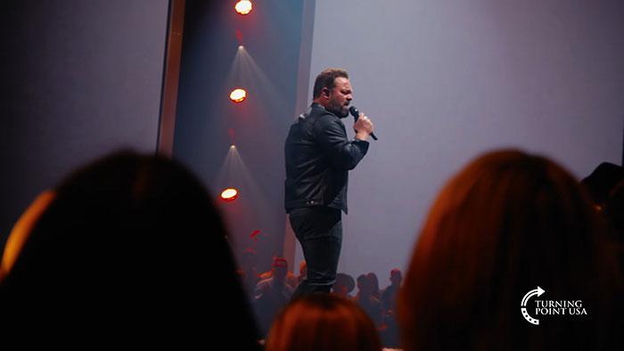 Kid Rock performing on stage at Turning Point USA’s alternative Super Bowl show with an audience in the foreground.